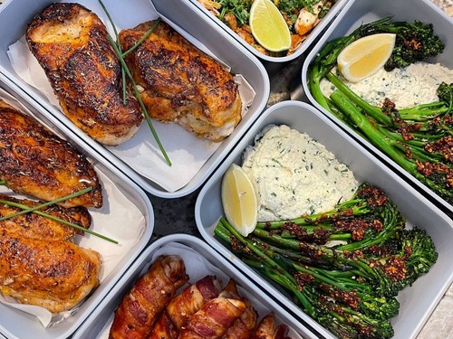 Prepared meals with roasted portions and green vegetables in glass containers.