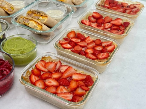 Glass meal prep containers filled with strawberry cheesecake baked oats topped with fresh sliced strawberries on a white surface.