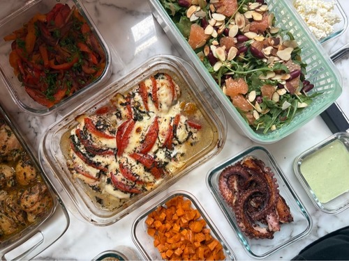 A collection of glass containers featuring tomato basil chicken, garlic seared octopus, roasted sweet potatoes, fajita-style peppers, and a vibrant salad with grapefruit and almonds.