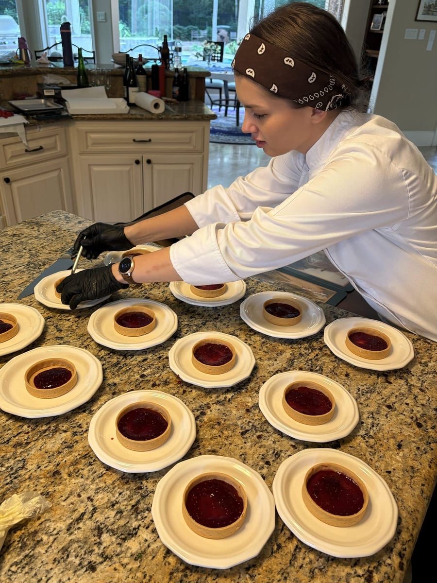 Chef Ana filling individual shortcrust tart shells with raspberry compote for the mini raspberry cheesecake tarts.