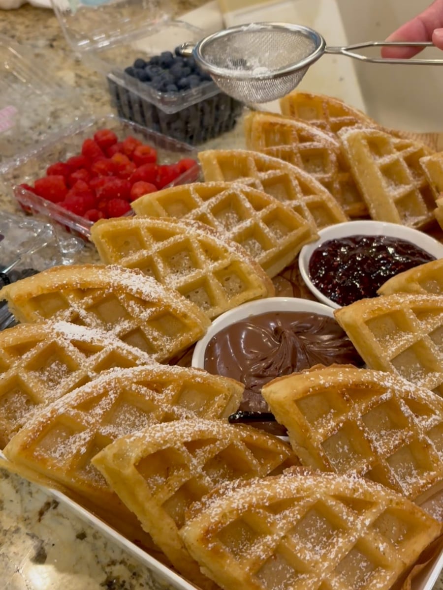 The Father's Day brunch waffle spread — golden Belgian waffles dusted with powdered sugar, fresh raspberries and blueberries, chocolate hazelnut spread and berry jam.