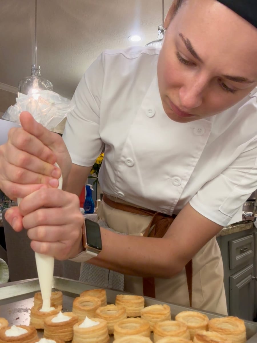 Chef Ana piping cream filling into puff-pastry vol-au-vent shells on a sheet tray.
