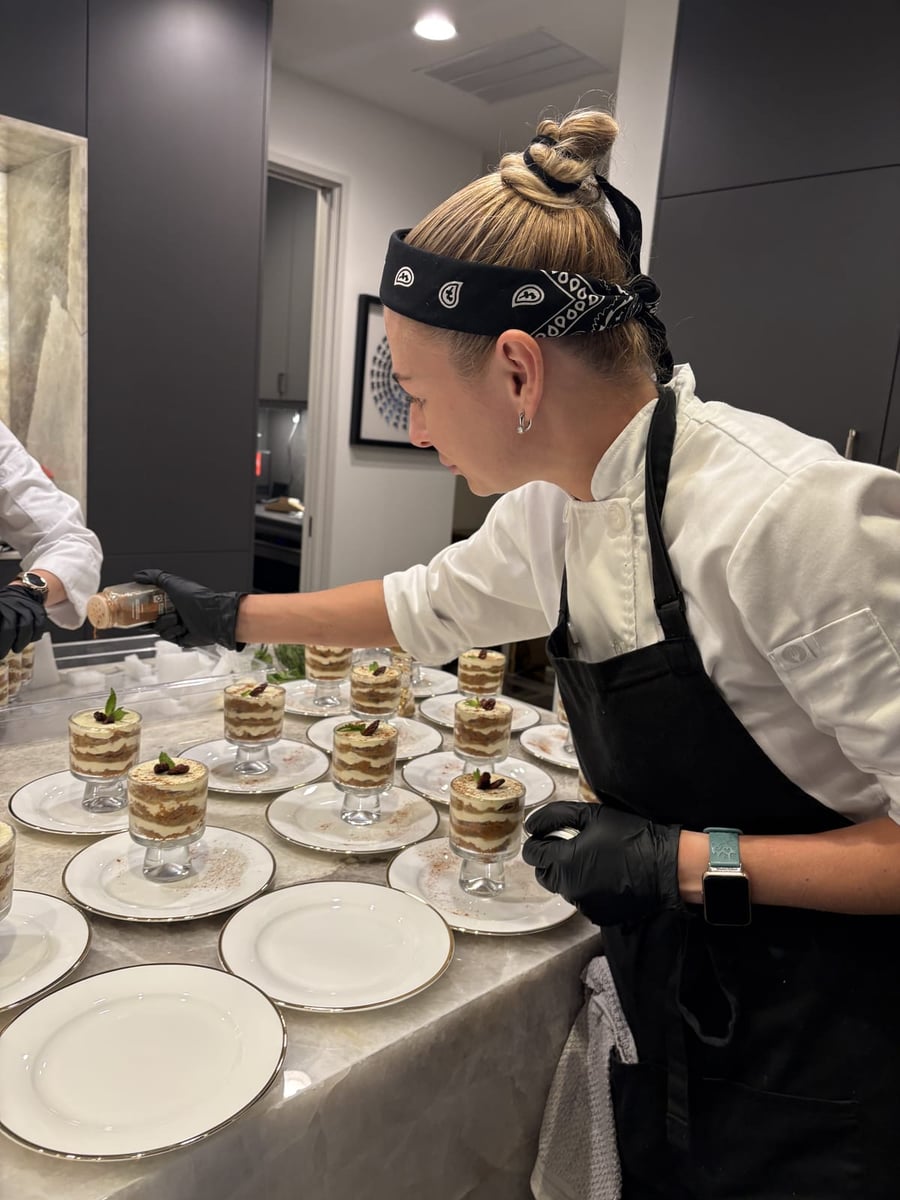 Chef Ana dusting cocoa over individual tiramisu parfait cups garnished with mint before service.
