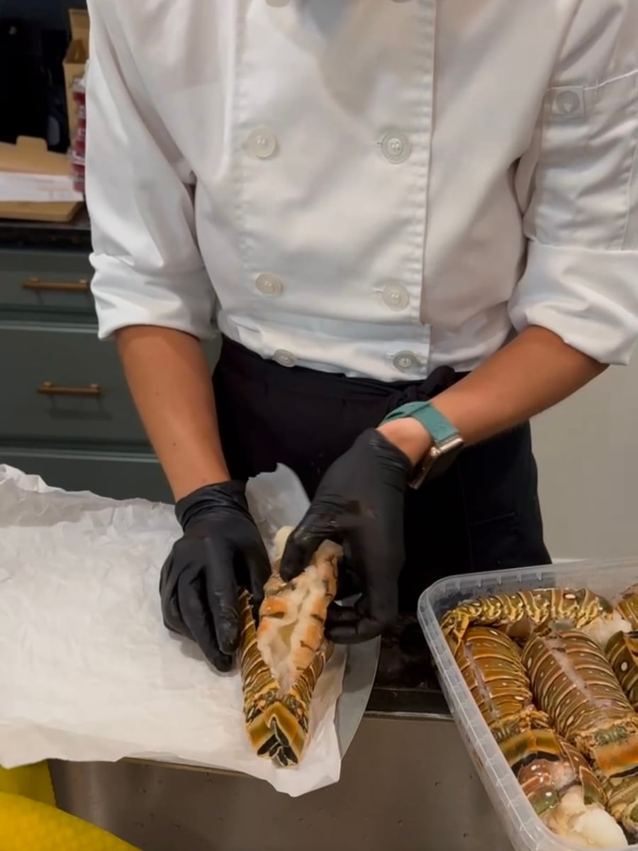 Chef Ana laying prepped lobster tails on a parchment-lined tray from a chilled tray of split spiny lobster tails.