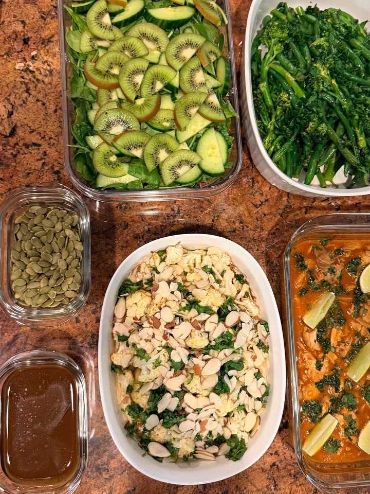 Glass containers featuring a kiwi cucumber salad, chili crisp green beans, harissa white fish with lemon, and a Mediterranean cauliflower and almond dish.