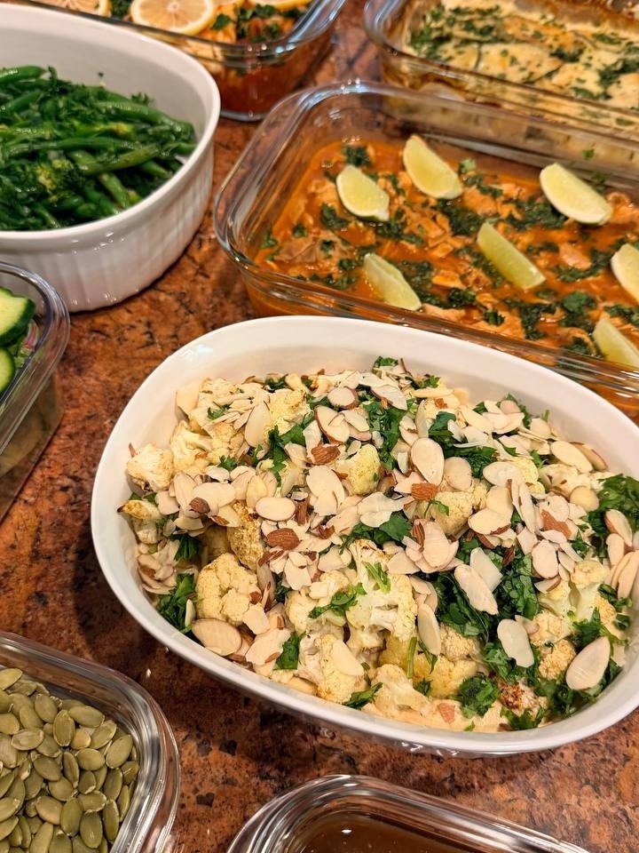 A spread of meal prep dishes including harissa cod with lime, mediterranean spiced cauliflower with almonds, and a creamy potato and zucchini gratin.