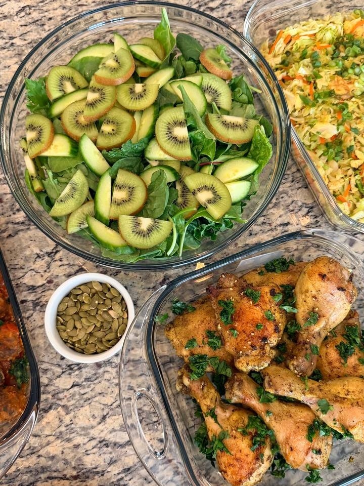 Glass containers featuring Lebanese-style baked chicken drumsticks and thighs garnished with fresh herbs alongside a vibrant fruit and vegetable salad.