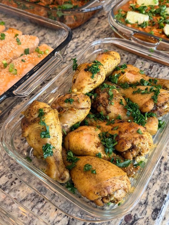A glass baking dish overflowing with golden roasted chicken drumsticks, seasoned with Mediterranean spices and generously garnished with fresh chopped green parsley.