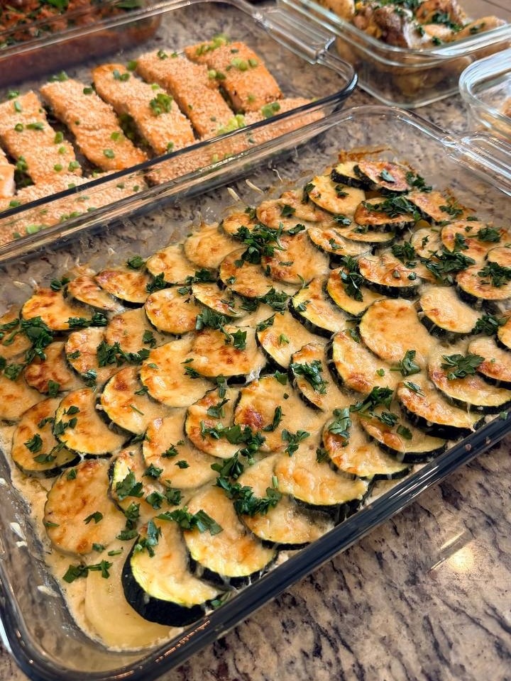 A glass baking dish filled with a layered potato, zucchini, and Gruyere gratin sits beside a container of sesame-crusted miso glazed salmon fillets.