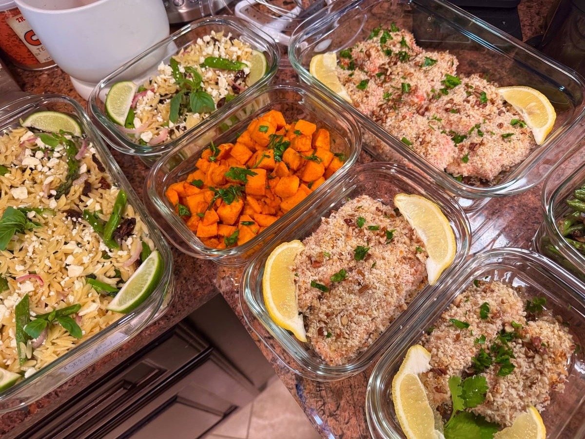 Glass meal prep containers filled with crispy pecan-crusted salmon, orzo pasta with sun-dried tomatoes and feta, and vibrant paprika-spiced sweet potato bites.