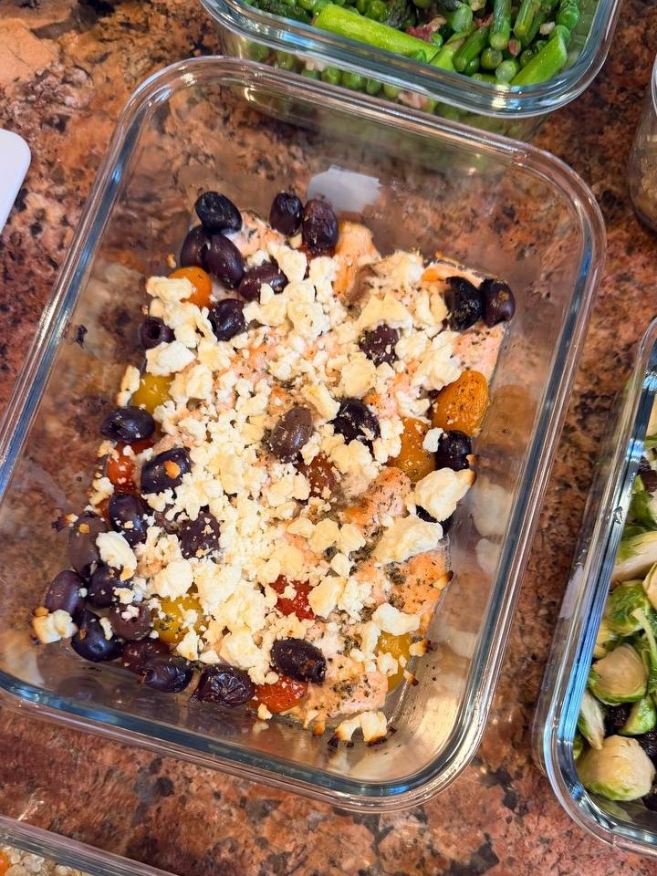 Glass meal prep containers filled with Mediterranean baked salmon bites topped with crumbled feta, black olives, and herbs, arranged on a marble surface.
