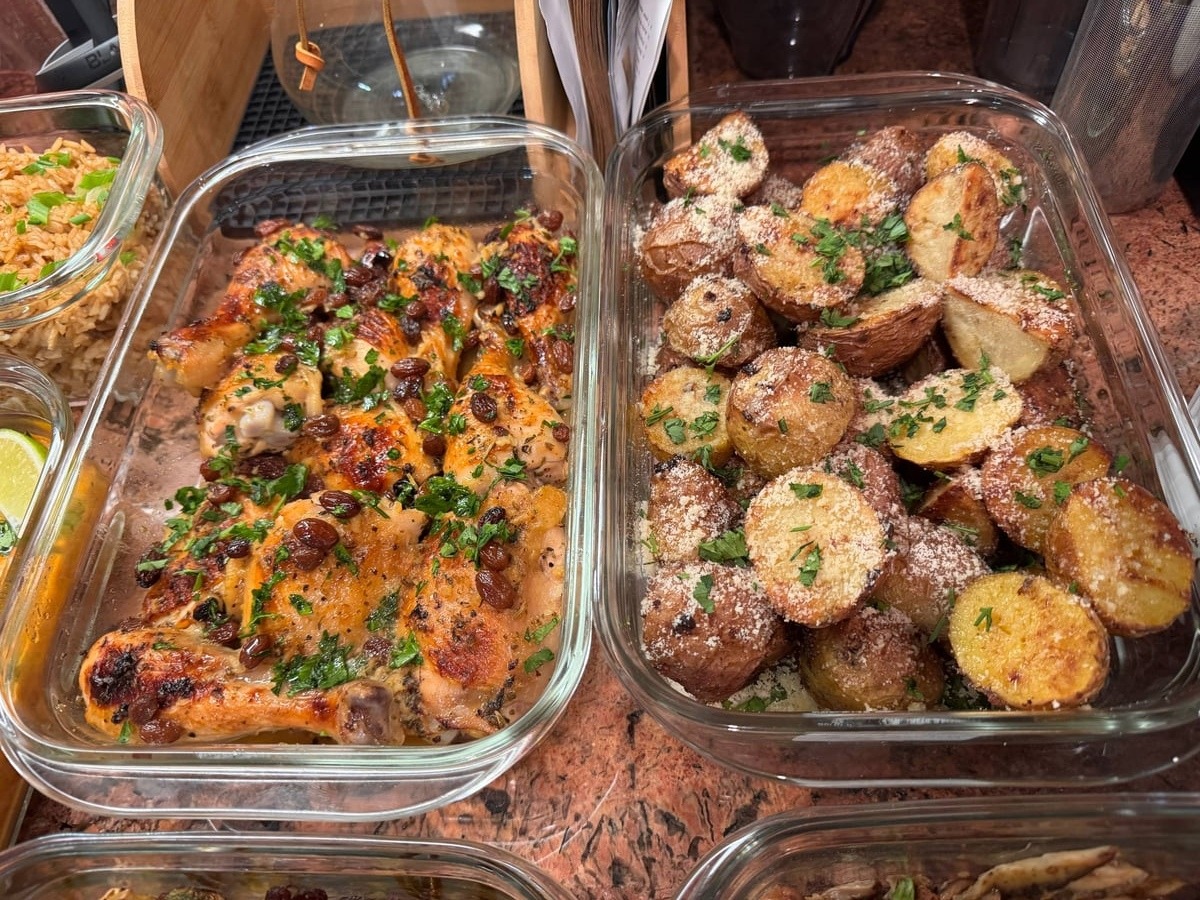 Glass containers hold orange cranberry baked chicken with fresh herbs and truffle parmesan baby potatoes, presented in organized, transparent meal prep dishes.
