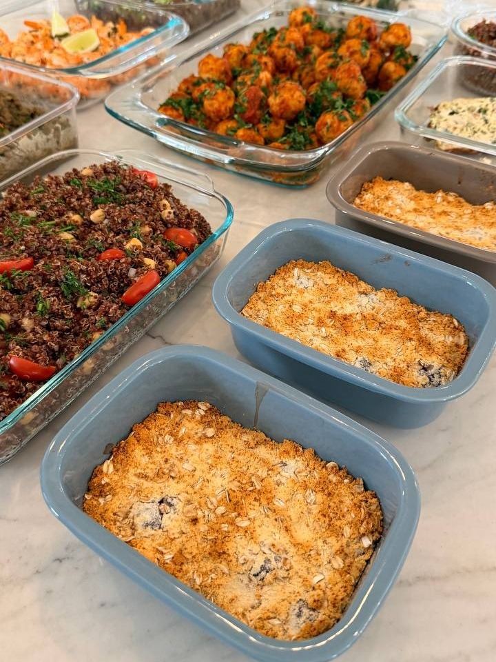 A collection of glass meal prep containers featuring Tuscan turkey meatballs, quinoa with tomatoes, ginger beef, and berry oat crumble bakes.