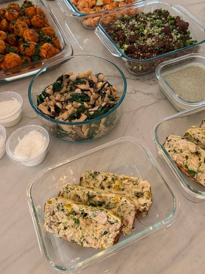 An assortment of glass containers filled with turkey meatballs, lime shrimp, ginger beef, sauteed spinach, egg bake, and various healthy prepared side dishes.