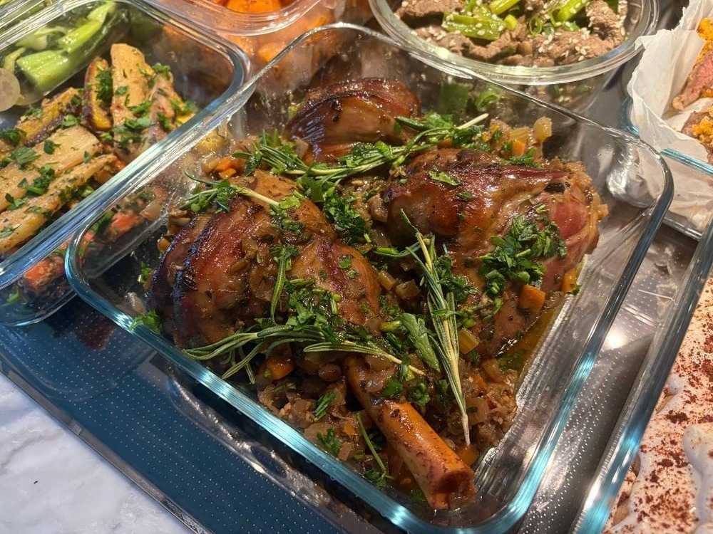 Braised lamb shanks with herbs and vegetables in a glass container.