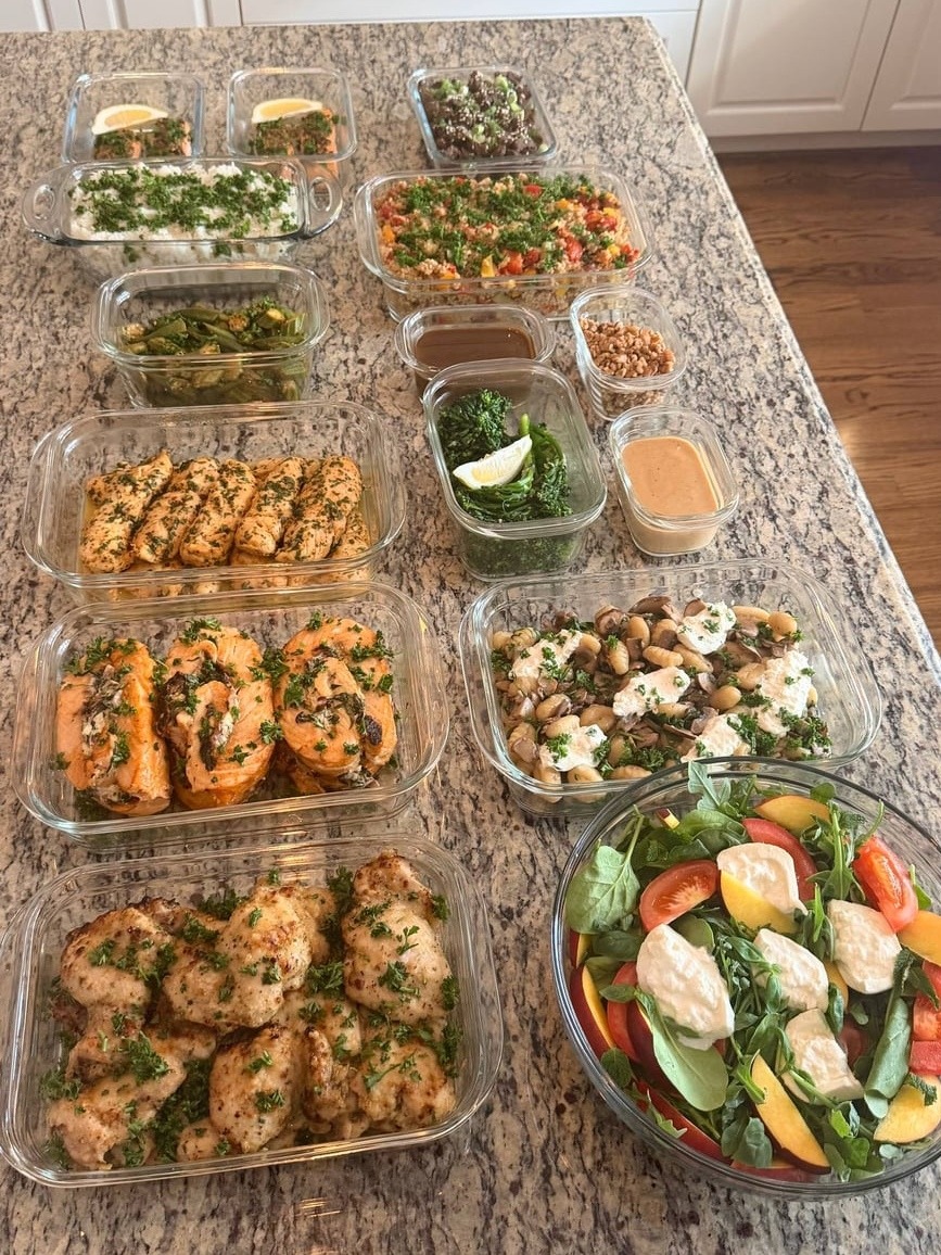 A collection of glass meal prep containers featuring Korean BBQ steak, honey lime chicken, salmon pinwheels, gnocchi, broccolini, and a fresh mozzarella peach salad.