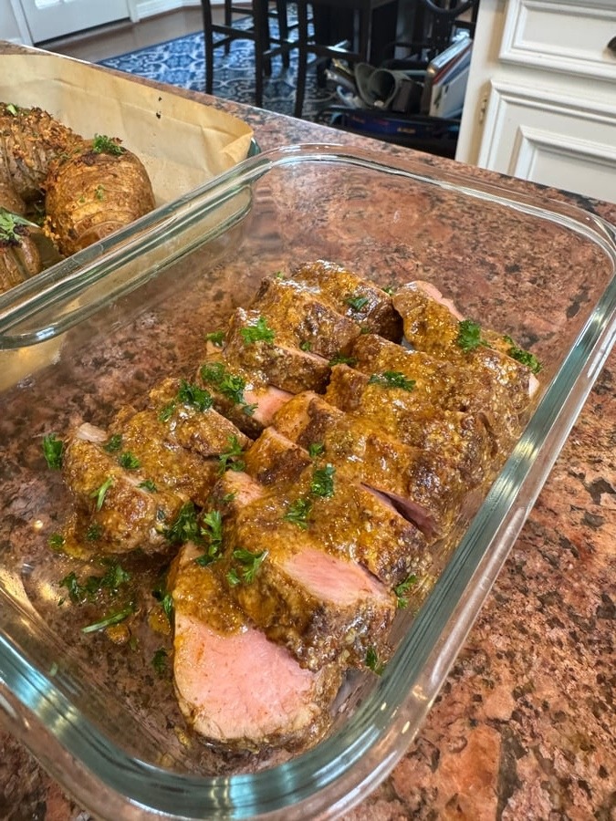 Sliced pork tenderloin coated in a rich maple mustard sauce, garnished with fresh parsley, next to a side of golden oven-roasted hasselback potatoes.