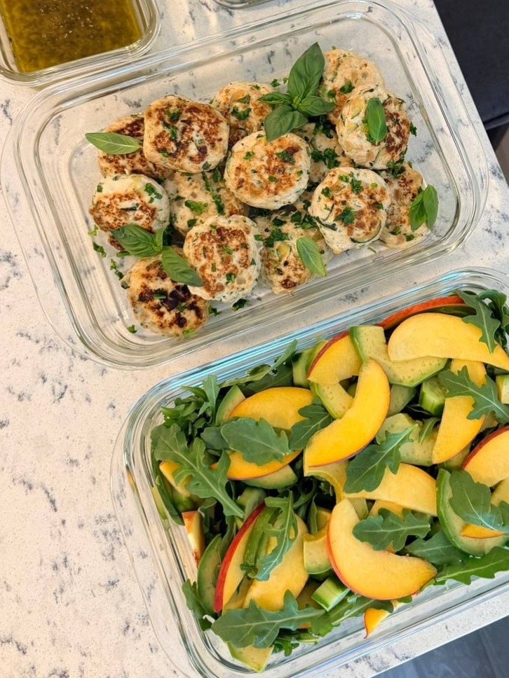Whole basil tops the seared chicken patties, with peach, avocado and cucumber layered through arugula beside them.