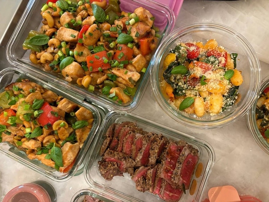 A variety of glass meal prep containers featuring sliced rosemary garlic filet mignon, cashew bell pepper chicken breast bites, and cherry tomato spinach seared gnocchi.
