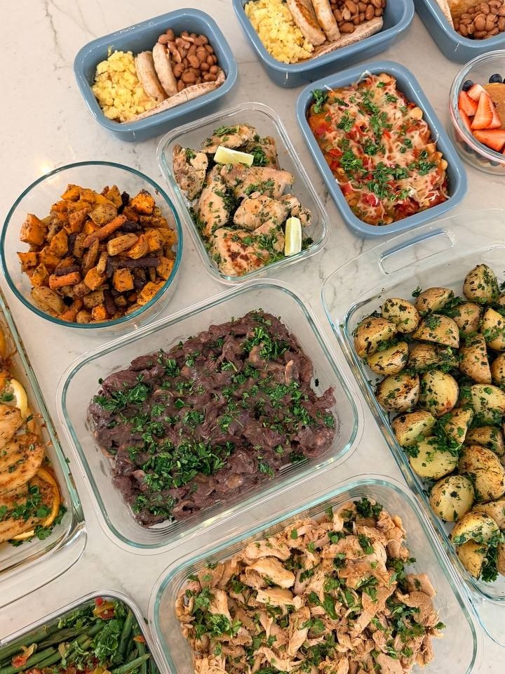 A variety of meal prep containers hold shredded chicken, beef sirloin, potatoes, green beans, and breakfast plates with eggs, turkey patties, and beans.