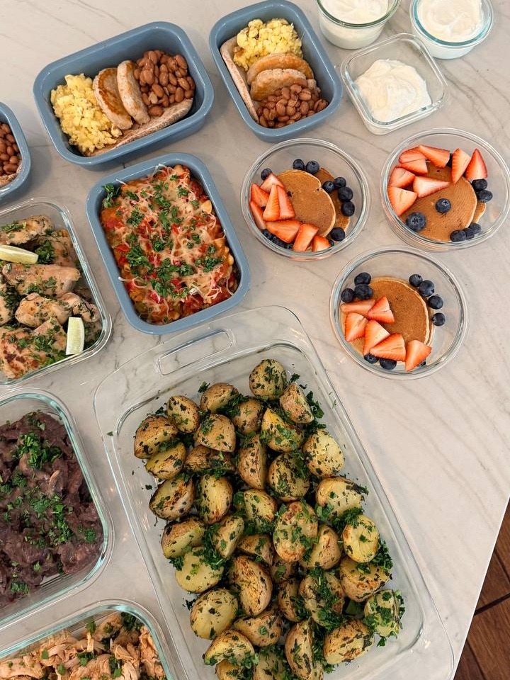A variety of meal prep containers featuring protein oat pancakes, turkey patties with eggs, lime cilantro chicken, beef sirloin, and boiled gold potatoes.