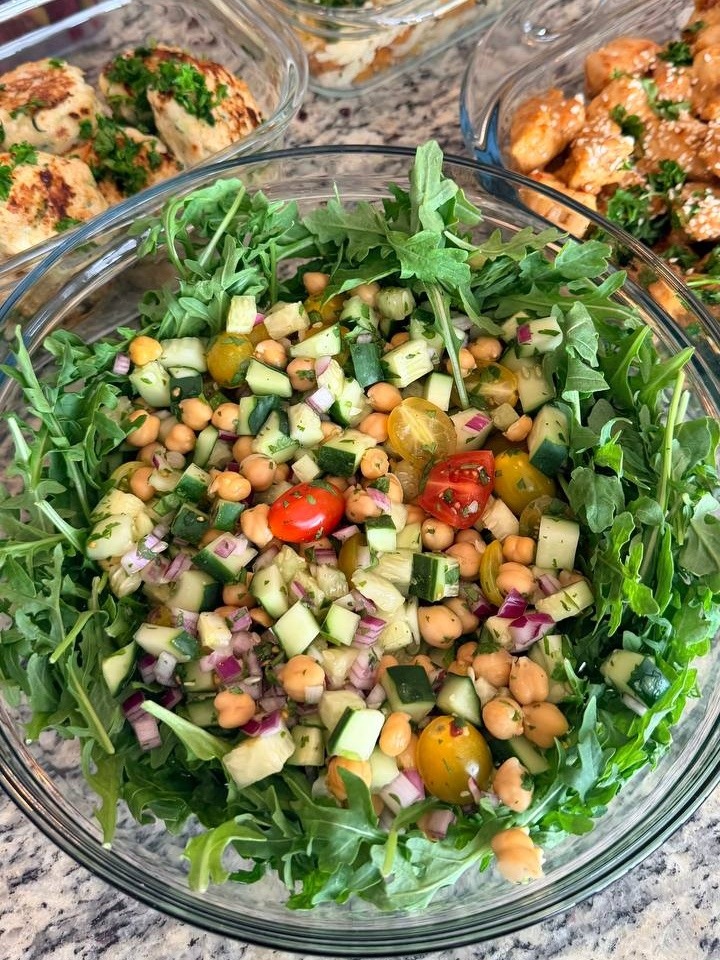 Mid-East chickpea salad with cucumbers, cherry tomatoes, and red onion served over fresh arugula, perfect for nutritious meal prep.