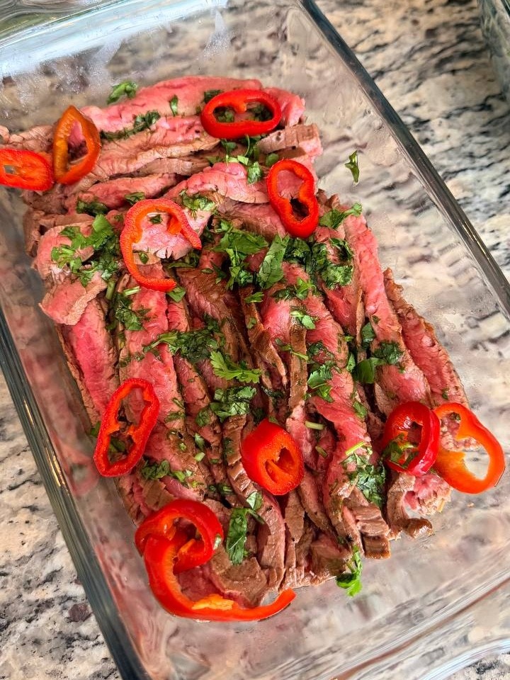 Thinly sliced Vietnamese skirt steak garnished with fresh chili rings and herbs, prepared for an elegant private chef dinner.