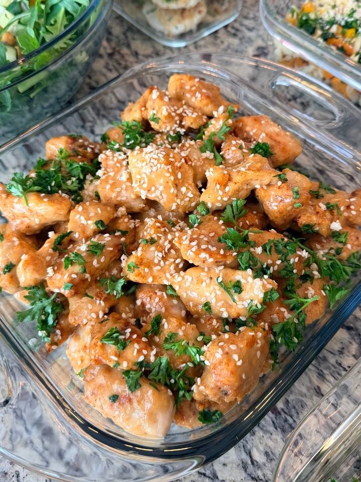 Glass meal prep containers filled with orange glazed crispy chicken bites, zucchini turkey fritters, roasted cauliflower with greens, and butternut orzo salad.