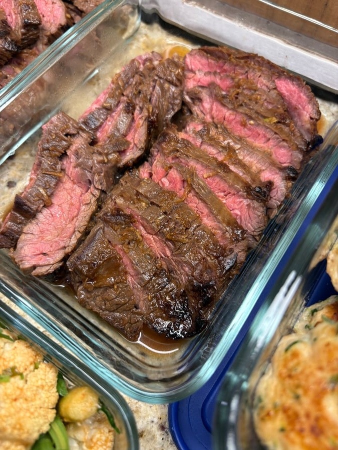 A glass storage container holding thinly sliced Vietnamese skirt steak with a vibrant pink interior, served in a lime agave vinaigrette glaze.