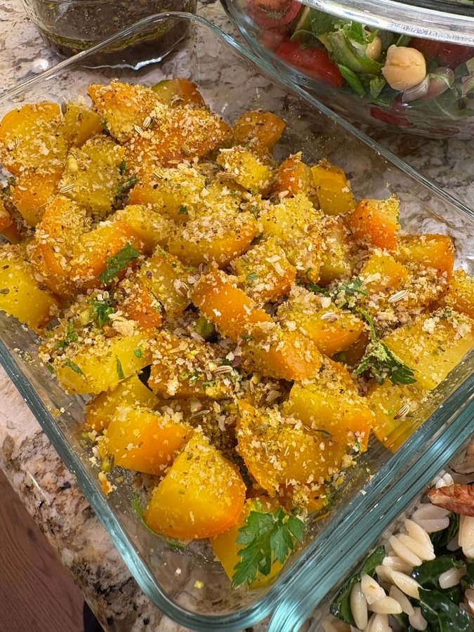 A glass container filled with vibrant roasted golden beets generously coated in crunchy pistachio dukkah, fresh herbs, and aromatic toasted spices.