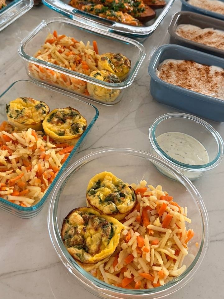 Glass meal prep containers filled with spinach feta egg bites and shredded carrot baked oats on a marble countertop.