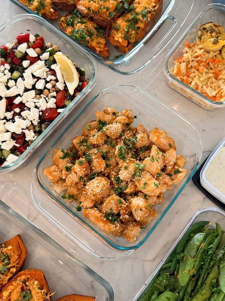 Glass containers featuring orange glazed chicken, Mediterranean chickpea salad, stuffed sweet potato boats, and garlic seared green beans and sugar peas.