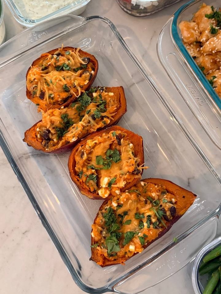 A glass dish features four halved sweet potatoes stuffed with a blend of black beans, cottage cheese, and herbs, arranged neatly for service.