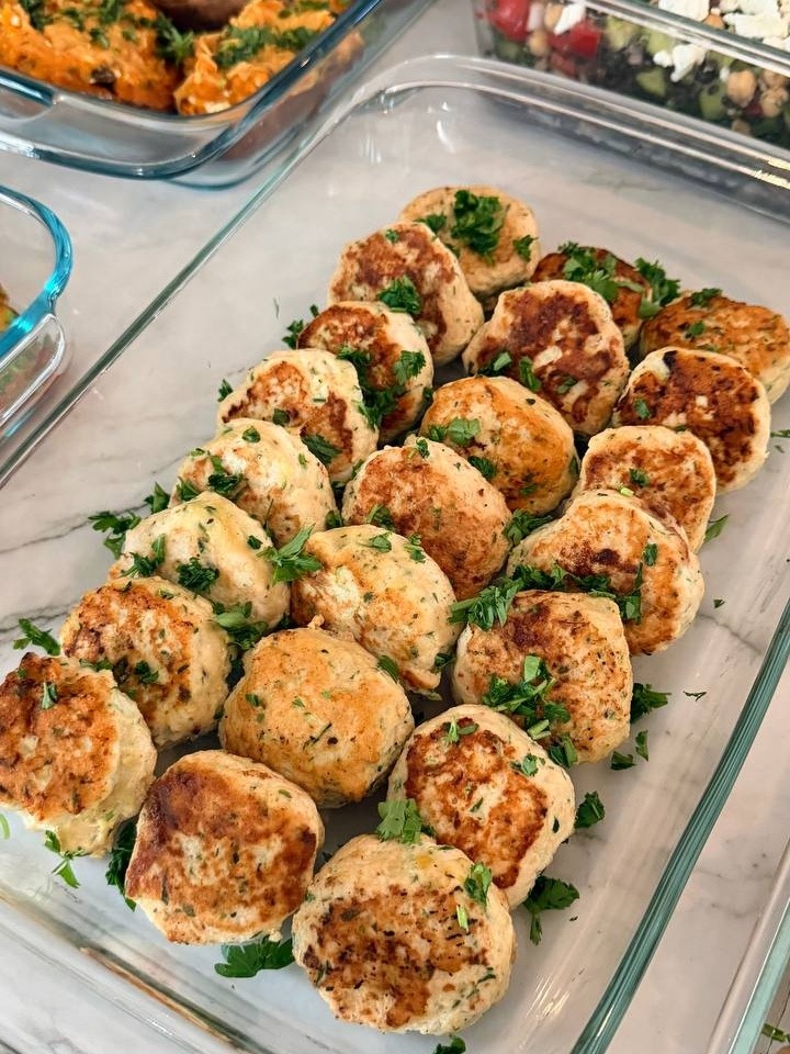 A glass baking dish filled with golden-brown zucchini turkey fritters, garnished with fresh green parsley and arranged in neat rows for easy serving.