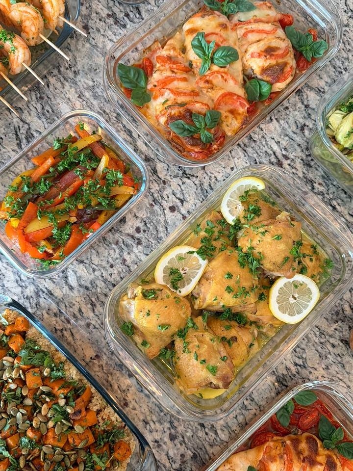 Glass containers featuring paprika lime shrimp, tomato basil caprese chicken, turmeric chicken thighs, fajita peppers, and roasted sweet potato quinoa on a granite surface.