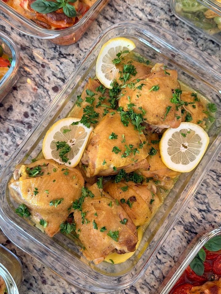 A glass container features golden saffron turmeric baked chicken thighs garnished with fresh lemon slices and chopped parsley, served alongside Caprese chicken and Brussels sprouts.