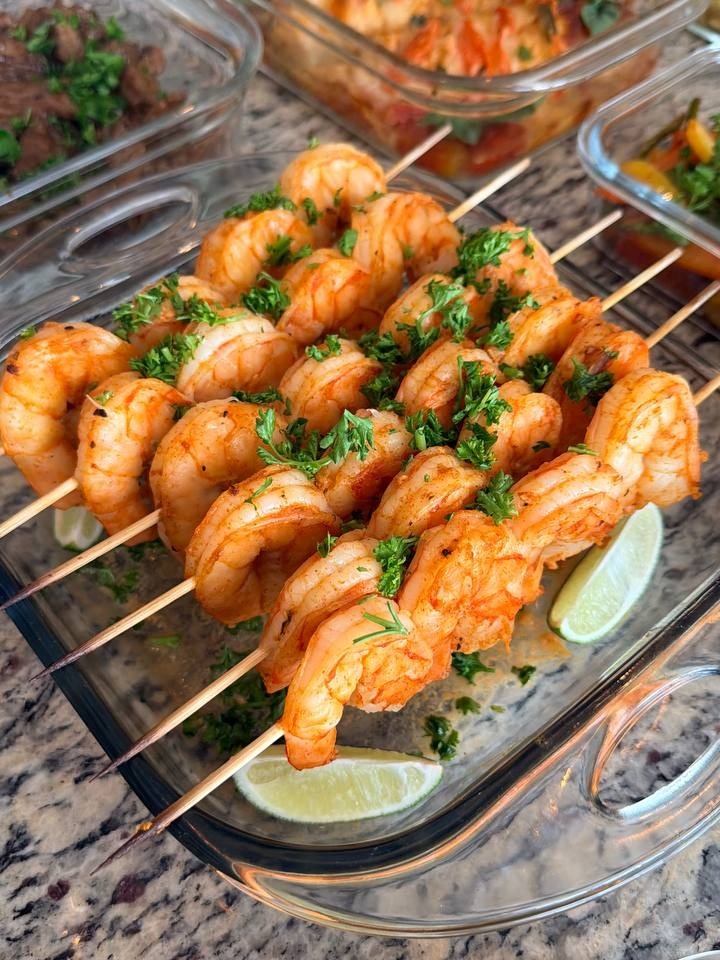 Grilled paprika lime shrimp skewers arranged in a glass rectangular dish, garnished with fresh chopped parsley and served with vibrant lime wedges.