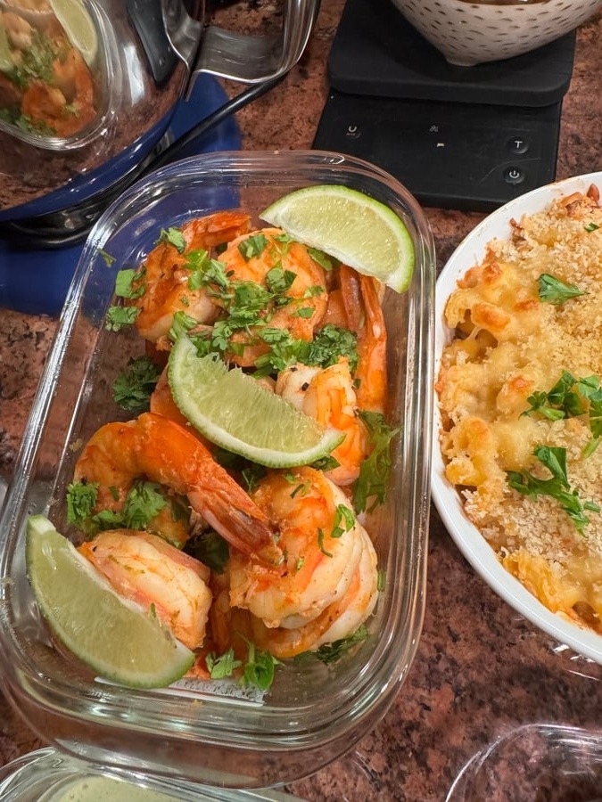These savory, pan-seared shrimp are beautifully presented with a vibrant garnish of fresh cilantro and lime wedges alongside a hearty portion of baked pasta.