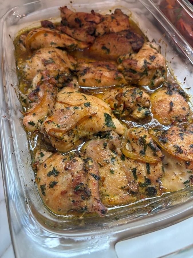A glass baking dish filled with golden-brown saffron turmeric baked chicken thighs, seasoned with fresh herbs and cooked in a savory pan sauce.