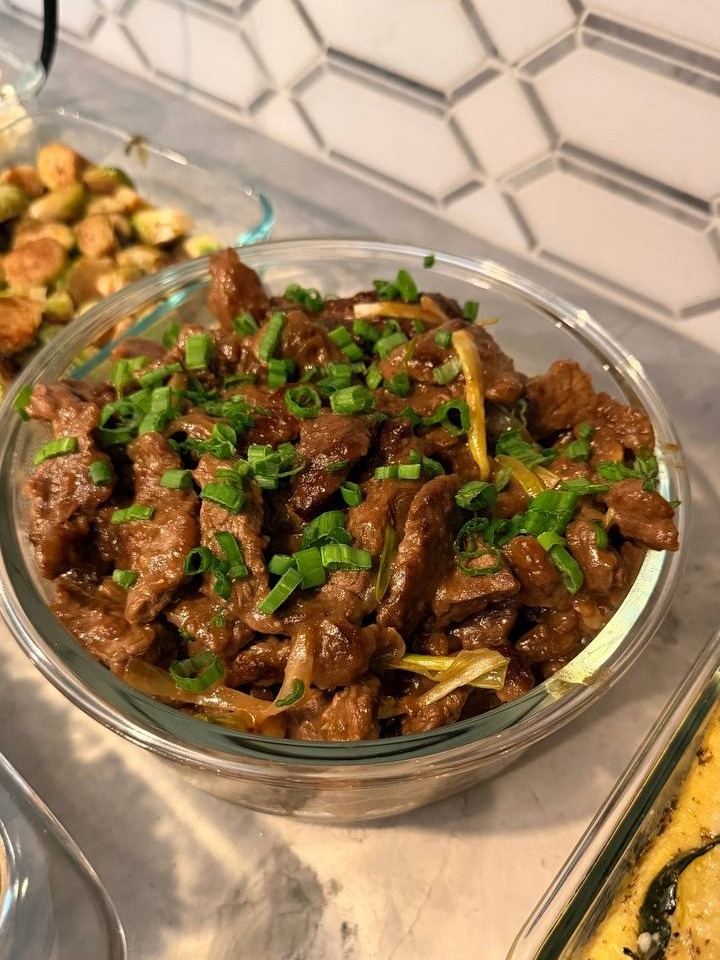 A glass bowl filled with savory Chinese beef and onion stir fry, garnished with vibrant green chopped chives and served in a clear container.