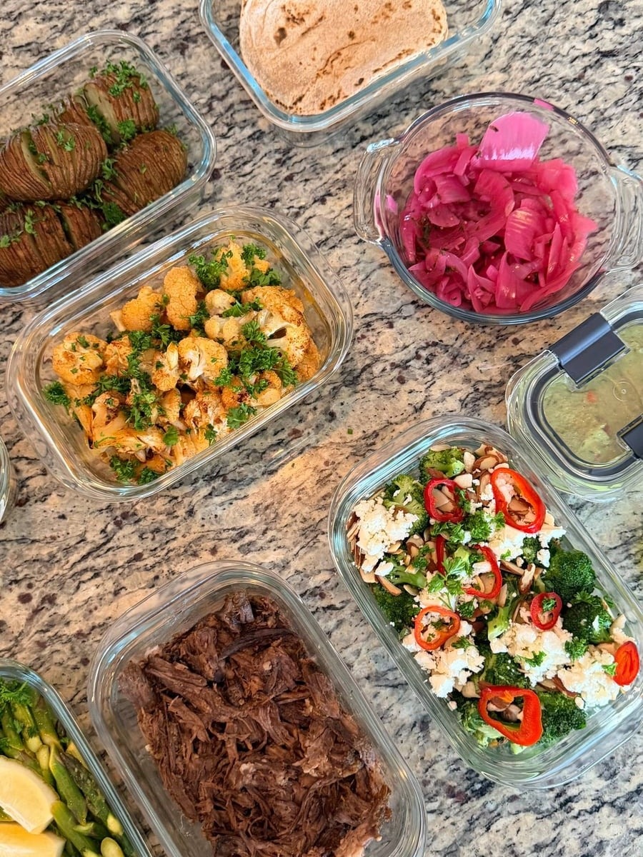 Glass containers featuring Mexican shredded beef, whole wheat tortillas, pickled onions, roasted honey lime cauliflower, hasselback potatoes, broccoli, and ginger asparagus stir-fry.
