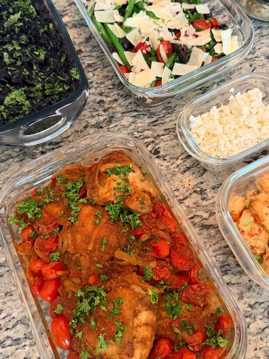 A glass container features zaatar seasoned chicken thighs nestled among roasted cherry tomatoes, garnished with fresh parsley and served in a clear rectangular dish.