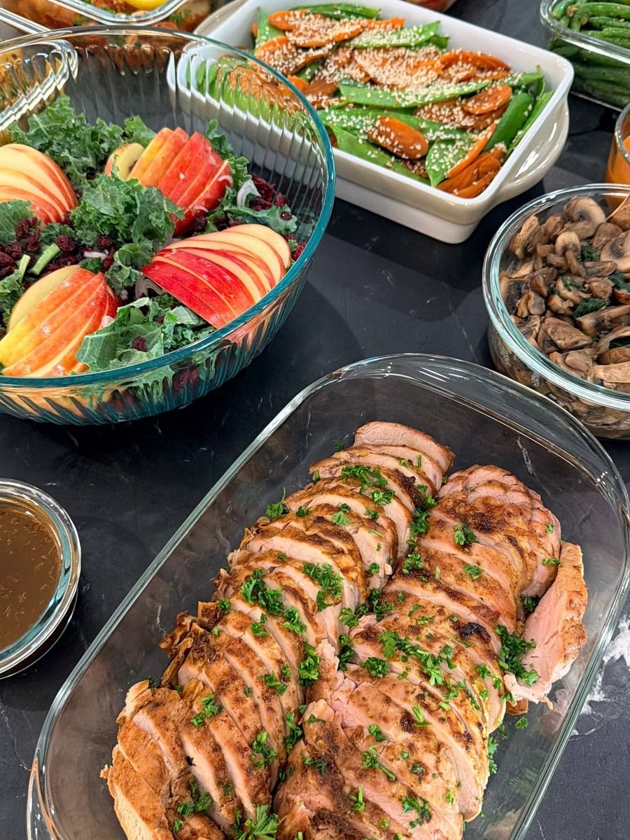 A glass serving dish containing sliced paprika-baked pork tenderloin garnished with chopped parsley, served with a side of rustic mango dipping sauce.