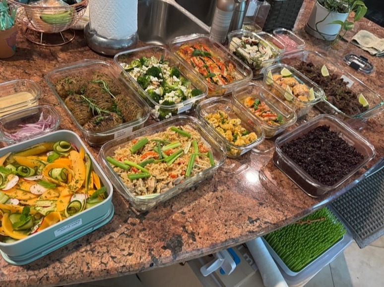 A variety of glass meal prep containers filled with garlic salmon bites, chicken pad thai, shredded beef, roasted potatoes, and a fresh melon salad.