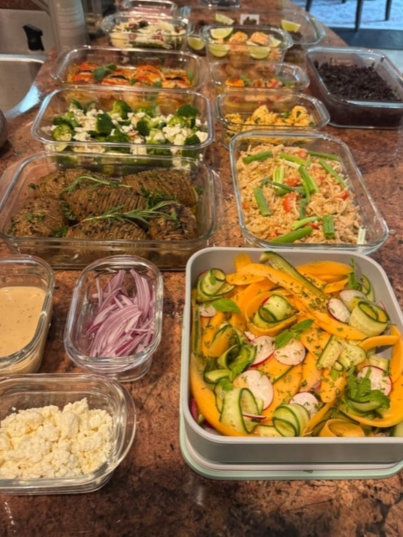 A collection of glass meal prep containers featuring tomato basil chicken, garlic rosemary potatoes, pad thai, and a vibrant melon cucumber radish salad.