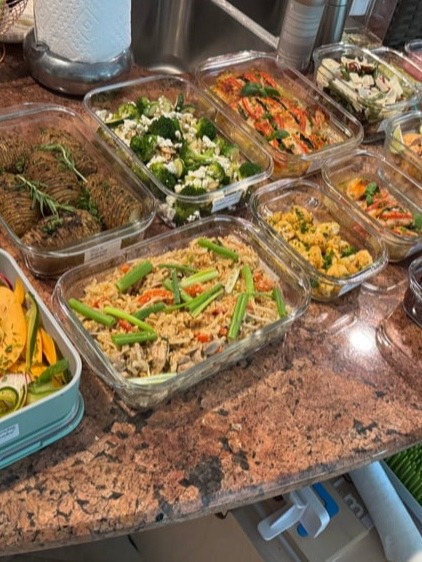A variety of glass meal prep containers filled with garlic salmon bites, chicken pad thai, shredded beef, roasted potatoes, and a fresh melon salad.