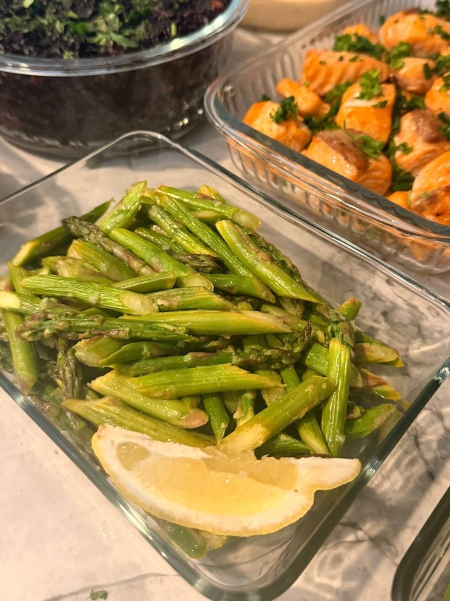 Glass meal prep containers filled with garlic salmon bites, cilantro almond black rice, and ginger garlic asparagus stir-fry garnished with a fresh lemon wedge.