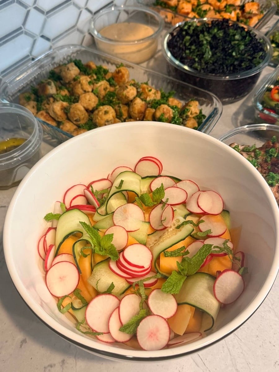 A large white bowl filled with a refreshing melon, cucumber, and radish salad garnished with sprigs of fresh mint and a light lemon vinaigrette dressing.