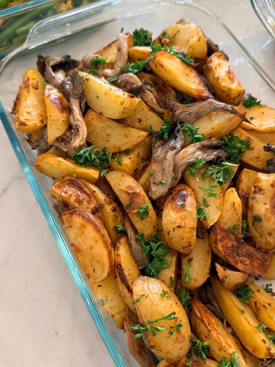 A glass container filled with roasted golden fingerling potatoes and earthy oyster mushrooms, finished with a vibrant sprinkle of fresh green parsley garnish.