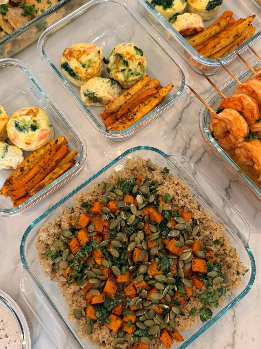 Glass containers featuring shrimp broccoli omelets, roasted sweet potato bites, paprika lime shrimp skewers, roasted sweet potato cilantro quinoa, and saffron turmeric chicken.